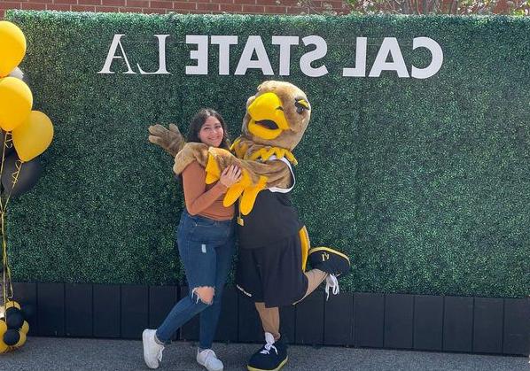 Eddie the Golden Eagle lifts leg while posing with a student.