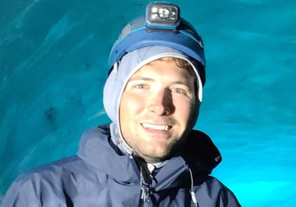 A man stand behind ice glaciers smiling.