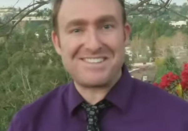 A man wear a purple shirt with a tie smiling. 