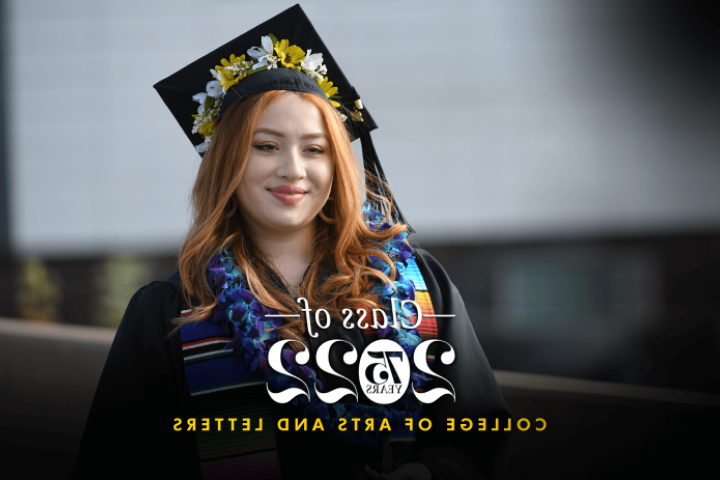 Student wearing a cap and gown smiles for a photo during the College of Arts and Letters commencement ceremony.