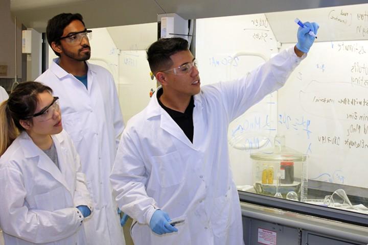 students in lab coats and goggles in lab working on formula