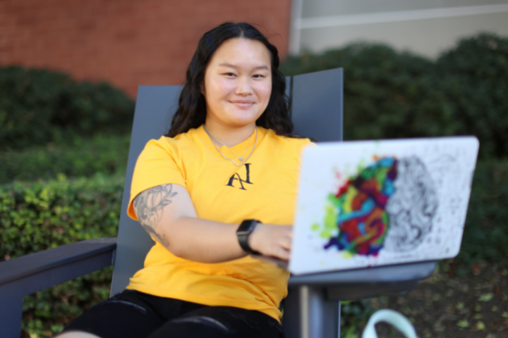 Female student sitting in lounge chair outside with open laptop.