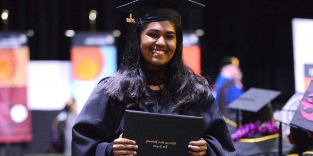 A graduate of Cal State LA at graduation, smiling, holding her diploma