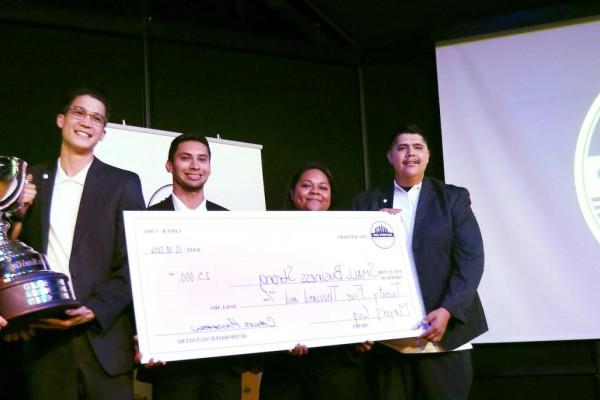 Group of Cal State LA students in business attire on a stage holding a large check near a screen that says "2016 Mayor's Cup"