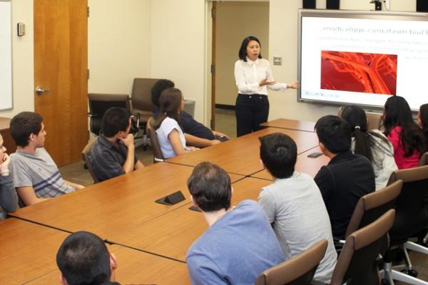 Group of Cal State LA students in a classroom around a conference table facing a projector screen as a lecturer teaches.