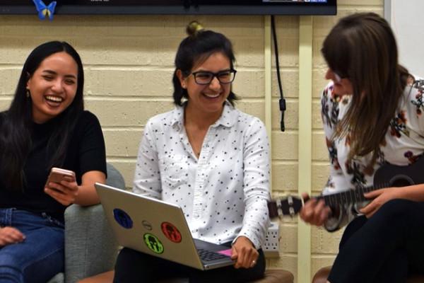 Three female students smiling, one playing a ukalele. 