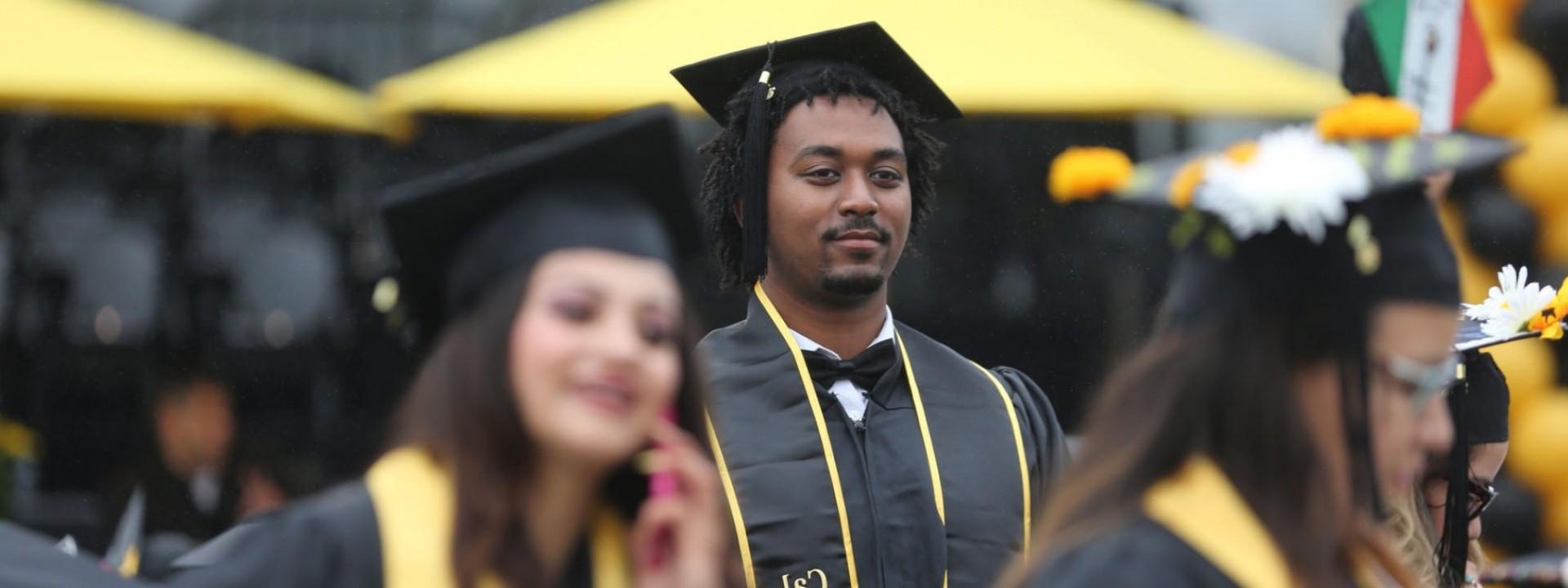 Image of a Black male student in Commencement regalia with a stoic expression on his face. 